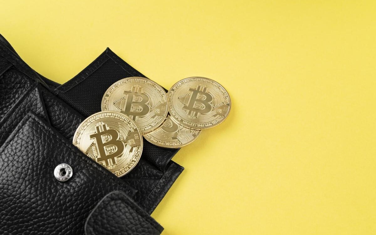 Gold Bitcoin coins tucked into a black leather wallet against a yellow background.